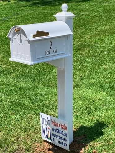 A white mailbox with a sign on it in a grassy area.