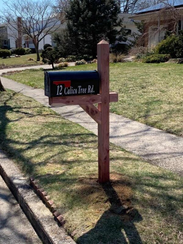 A Cedar Post/ Standard Mailbox & Installation with a sign on it in front of a house.